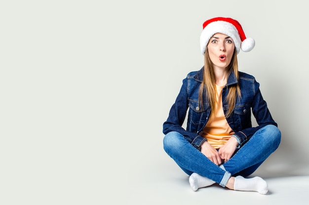 Surpris jeune fille portant un chapeau de père Noël sur fond clair