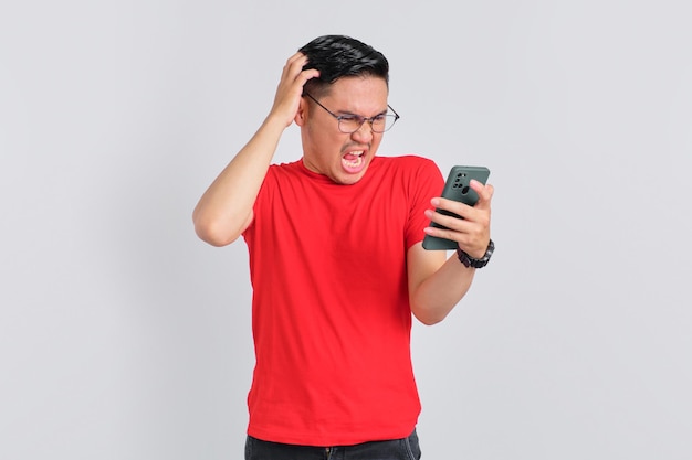 Surpris jeune homme asiatique regardant l'écran du téléphone mobile réagissant aux nouvelles en ligne isolé sur fond blanc