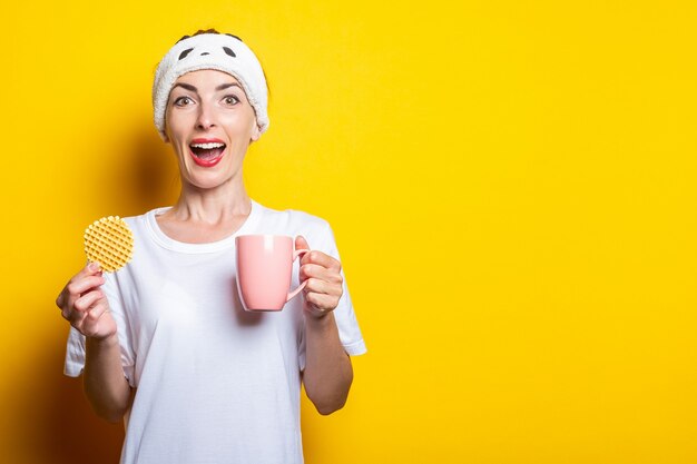 Surpris joyeuse jeune femme avec tasse de thé et gaufre belge sur fond jaune.