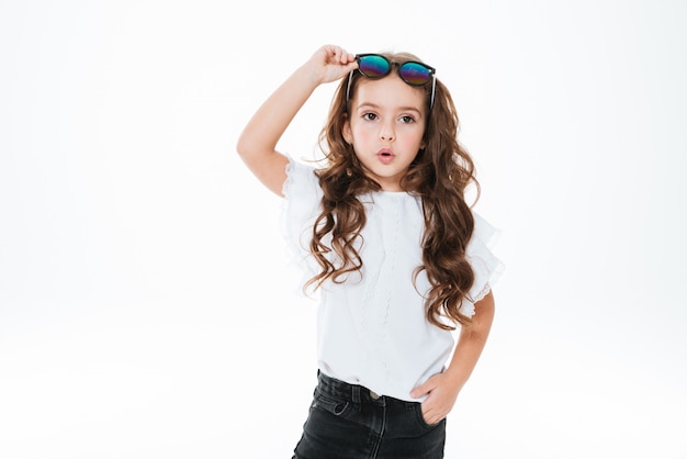 Surpris petite fille bouclée à lunettes de soleil debout et posant