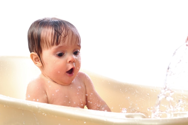 Surpris petite fille jouer avec enthousiasme avec des éclaboussures d'eau dans le bain