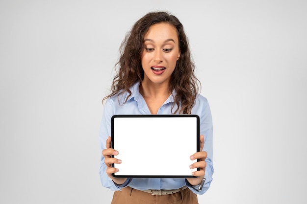 Surprise heureuse femme d'affaires caucasienne du millénaire montre une tablette avec un écran vierge