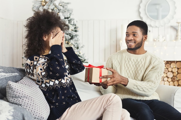 Surprise à Noël. Homme heureux surprenant sa petite amie avec un cadeau de Noël, femme excitée fermant les yeux, espace de copie