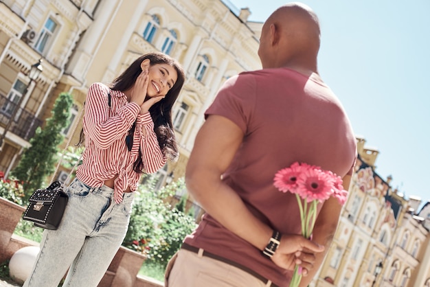 Surprise romantique jeune couple diversifié debout sur le petit ami de la rue de la ville tenant un bouquet de