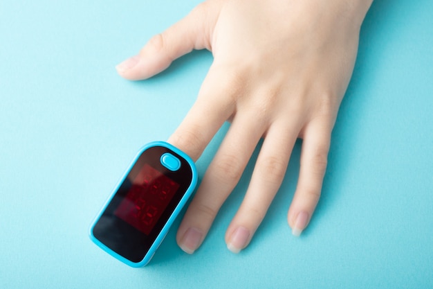 Surveillance de la saturation en oxygène du sang avec un appareil spécial sur un doigt féminin sur fond bleu