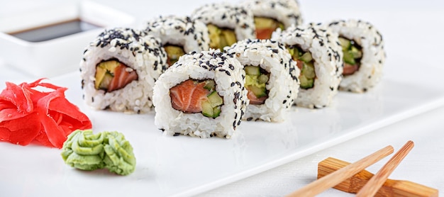 Sushi au saumon sur une plaque blanche avec des baguettes de soja gingembre wasabi sur fond blanc