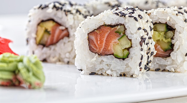 Sushi au saumon sur une plaque blanche avec des baguettes de soja gingembre wasabi sur fond blanc