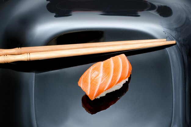 Sushi et baguettes sur une plaque noire.