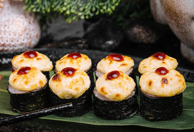 Sushi chaud servi roulé dans des feuilles de nori avec du gingembre et du wasabi sur une plaque en pierre noire