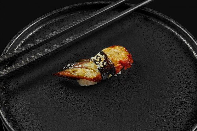 Sushi classique à l'anguille et au riz sur une plaque en céramique noire avec des baguettes élégantes noires. Cuisine japonaise traditionnelle. Photo pour le menu