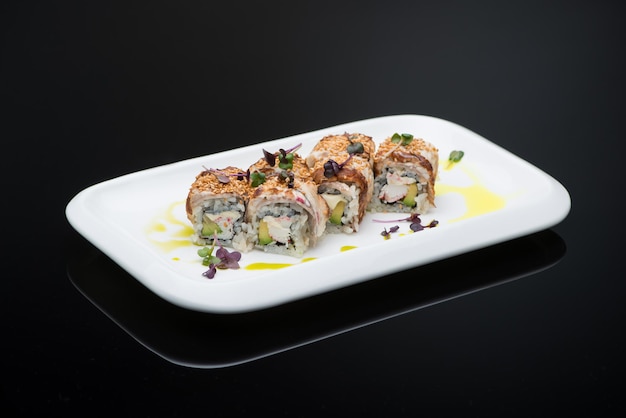 Sushi dans une assiette sur fond noir avec reflet. rouleau de poisson