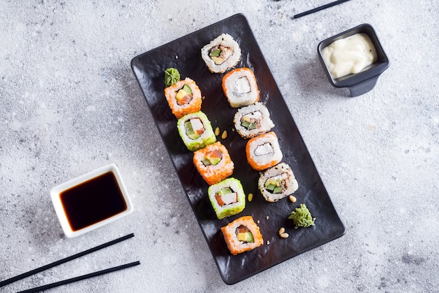 Sushi frais sur ardoise noire avec bâtons en métal, sauce sur pierre