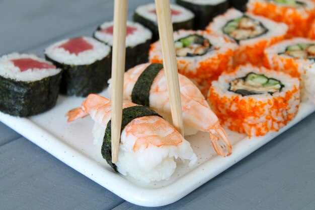 Sushi frais mis maki et rouleaux sur table en bois. Baguettes tenant nigiri aux crevettes