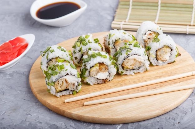 Sushi japonais maki à l'oignon vert sur une planche de bois sur béton gris