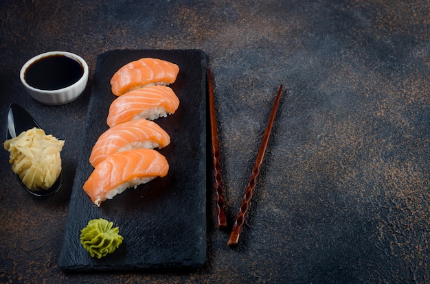 Sushi nigiri savoureux au saumon sur plaque de pierre noire avec sauce soja, gingembre, wasabi et baguettes