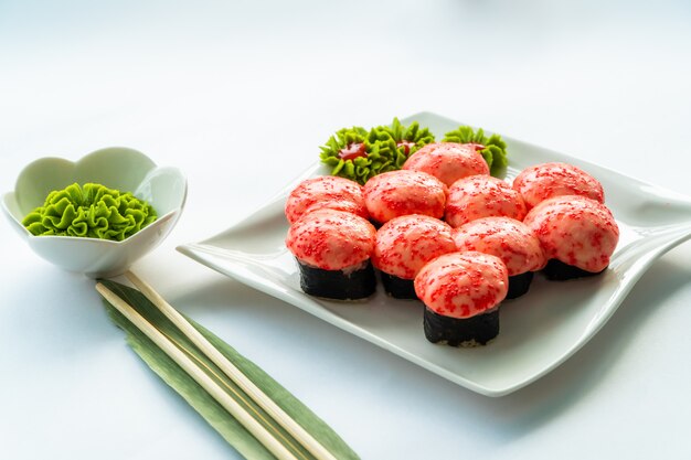 Sushi rouge sur une plaque blanche et une surface blanche avec du wasabi et des baguettes