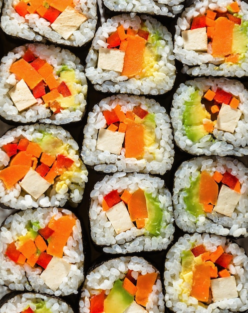 Sushi végétalien au tofu et légumes sur une table bleue avec sauce soja et graines de sésame noir