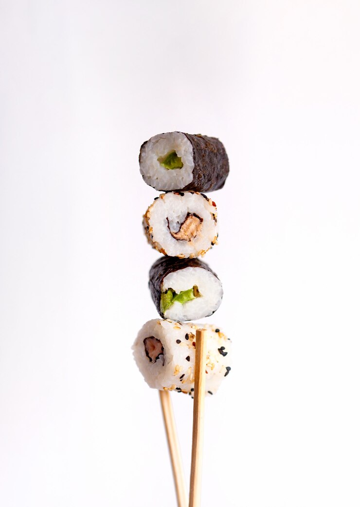 Sushi volant sur fond blanc, rouleaux de sushi savoureux, avocat et baguettes
