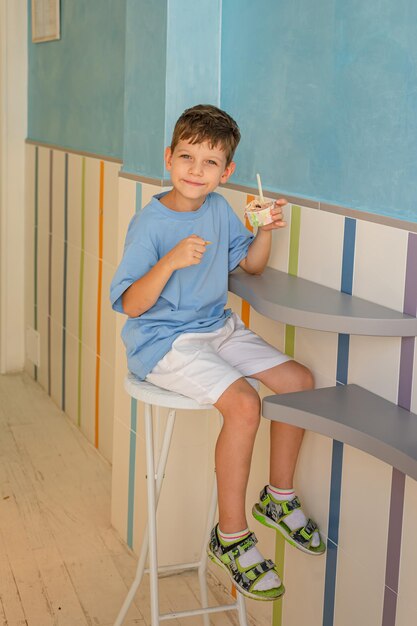 Sute garçon de 6 ans dans un t-shirt bleu mange de la glace avec une cuillère dans un verre dans une gelateria à Rome Tourisme de desserts traditionnels avec des enfants