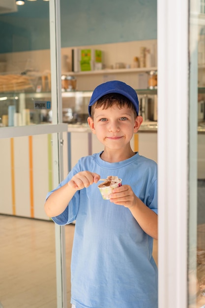 Sute garçon de 6 ans dans un t-shirt bleu mange de la glace avec une cuillère dans un verre dans une gelateria à Rome Tourisme de desserts traditionnels avec des enfants