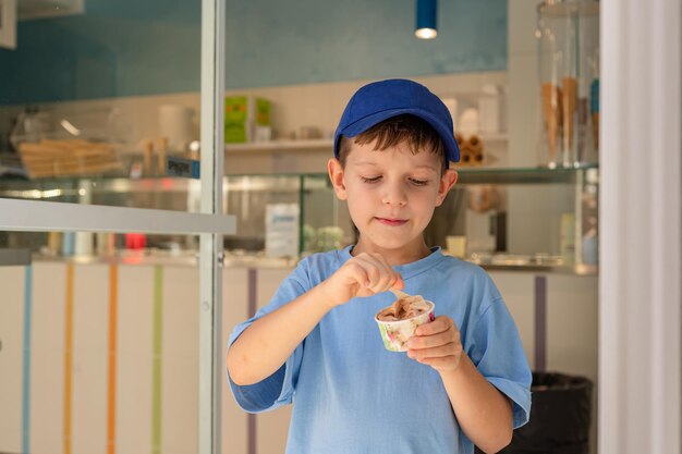 Sute garçon de 6 ans dans un t-shirt bleu mange de la glace avec une cuillère dans un verre dans une gelateria à Rome Tourisme de desserts traditionnels avec des enfants