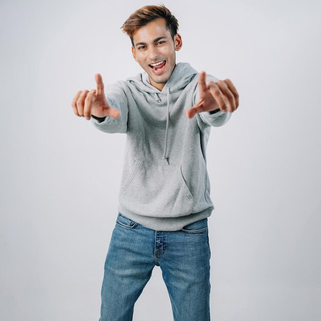 Sweat à capuche beau jeune homme indien pointant un mur gris isolé souriant