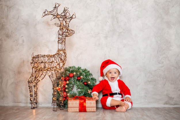 Sweet baby Santa est assis sur un plancher en bois avec un cadeau et une couronne de Noël