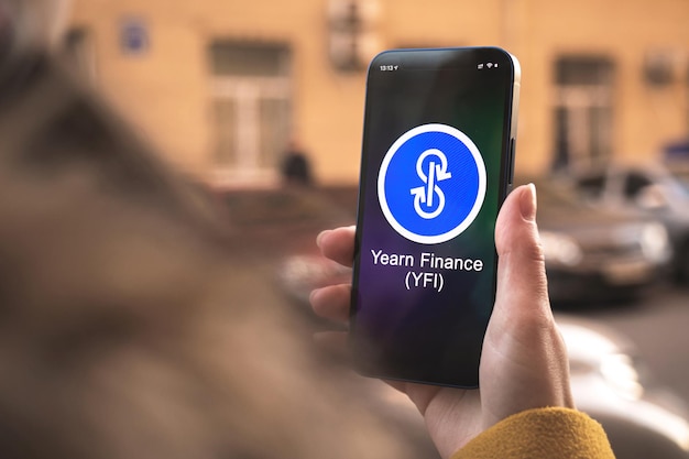 Symbole de crypto-monnaie Yearn Finance, logo. Concept commercial et financier. Main avec smartphone, écran avec gros plan sur l'icône crypto