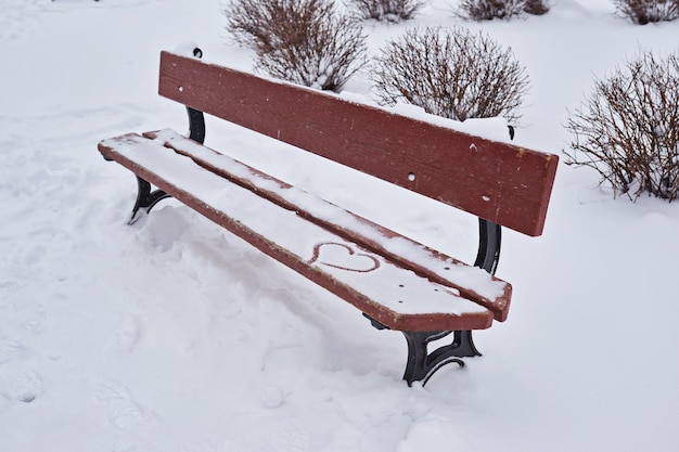 Un symbole du coeur est dessiné sur la neige blanche sur un banc orange