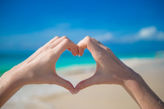 symbole du coeur fait par des mains féminines sur la plage