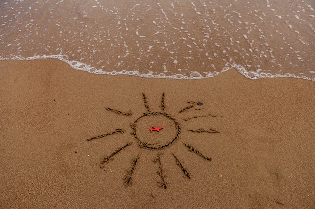 Symbole Du Soleil Et D'un Avion Au Bord De La Mer. Soleil Peint Sur Le Sable, Côte De La Mer, Figure D'un Avion Rouge, Vagues De La Mer.