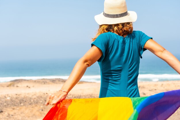 Symbole LGBT, une lesbienne méconnaissable de dos vêtue d'une robe verte agitant le drapeau au bord de la mer