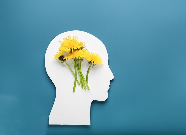 Symbole de tête humaine en papier et fleurs sur fond bleu Concept de la journée mondiale de la santé mentale