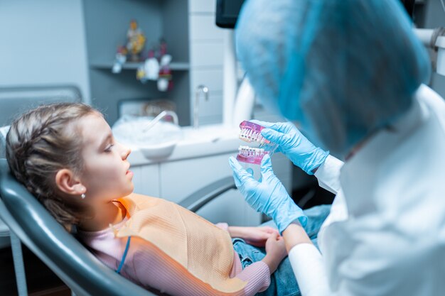 Sympathique dentiste orthodontiste éduquant une petite fille patiente à l'aide d'un modèle de dents avec brecets