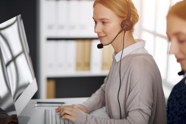 Sympathique femme d'affaires caucasienne parlant par casque dans un bureau ensoleillé Centre d'appels