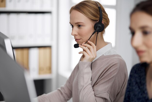 Sympathique femme d'affaires parlant par casque au bureau. Centre d'appels et groupe de personnes diverses dans les affaires.