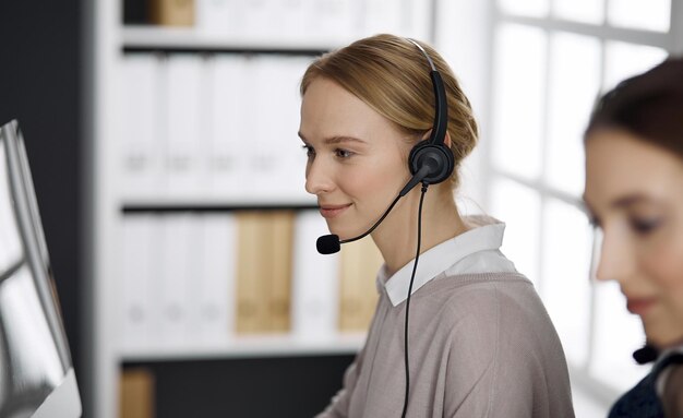 Sympathique femme d'affaires parlant par casque au bureau. Centre d'appels et groupe de personnes diverses dans les affaires.