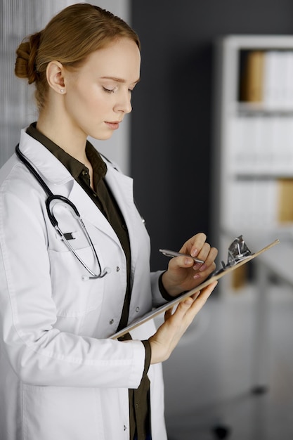 Sympathique femme médecin souriante utilisant un presse-papiers en clinique. Portrait d'une femme médecin sympathique au travail. Service médical à l'hôpital. Notion de médecine.