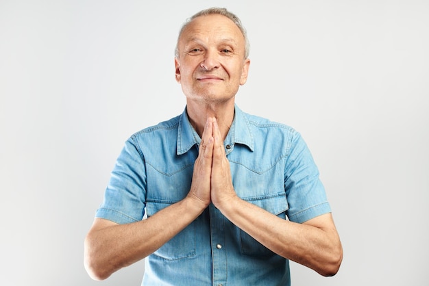 Sympathique gentille personne âgée attrayante souriante avec les mains jointes dans la prière reconnaissante pose isolée sur fond blanc