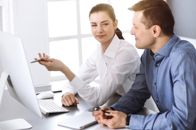 Sympathique homme d'affaires souriant et femme travaillant avec un ordinateur dans un bureau moderne. Headshot lors d'une réunion ou d'un lieu de travail. Travail d'équipe, partenariat et concept d'entreprise.