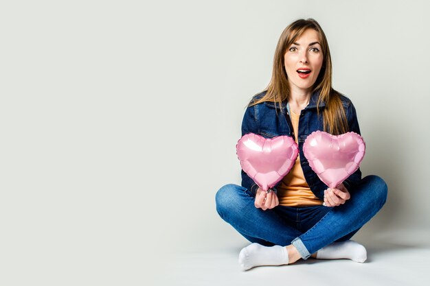 Sympathique jeune femme assise en tailleur tenant des ballons à air chaud en forme de coeur