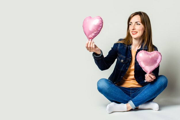 Sympathique jeune femme assise en tailleur tenant des ballons à air chaud en forme de coeur