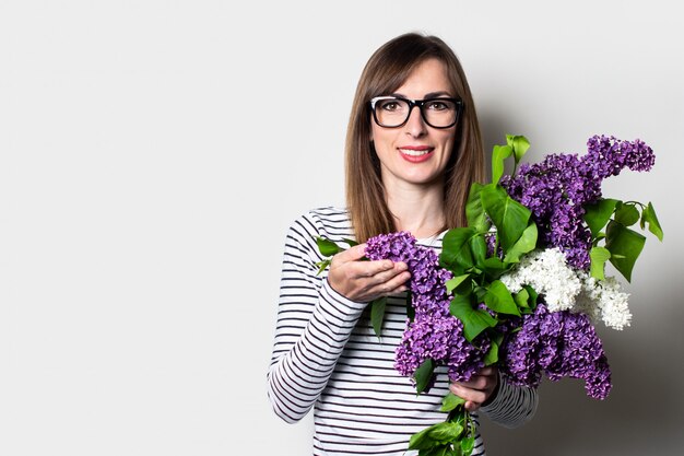 Sympathique jeune femme à lunettes détient un bouquet de lilas sur fond clair.