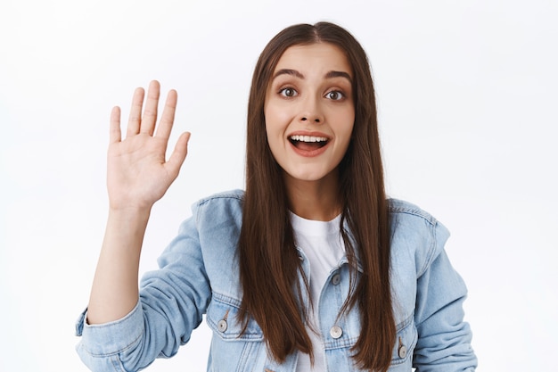 Sympathique jeune femme timide essayant de saluer une jolie fille dans un café pour obtenir son numéro, agitant la main dans un geste de salut ou de salut, souriante pleine d'espoir et mignonne, accueillant quelqu'un, fond blanc