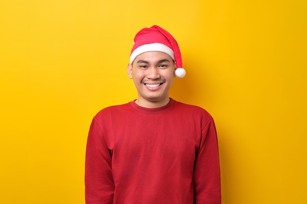 Sympathique jeune homme asiatique en bonnet de noel souriant joyeusement à la caméra sur fond de studio jaune célébration vacances de Noël et concept du nouvel an