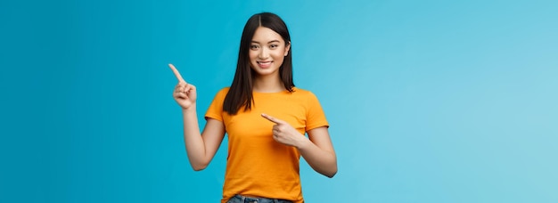 Sympathique joyeuse fille brune asiatique invitant à visiter le lien lieu intéressant pointant vers le haut à droite cor