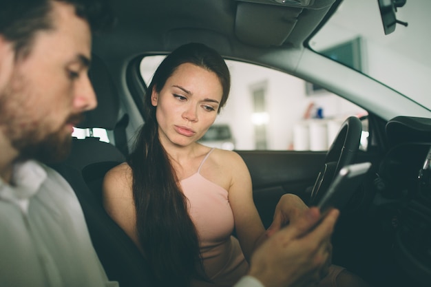 Sympathique vendeur de voitures parlant à une jeune femme et montrant une nouvelle voiture à l'intérieur du showroom Signature du contrat.