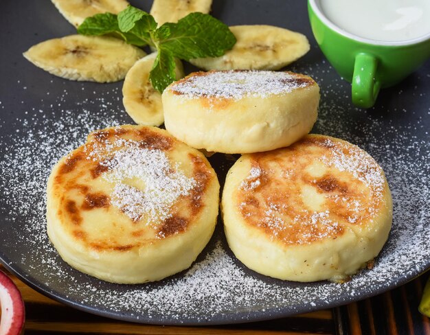 Syrniki ou crêpes au fromage avec sauce à la crème et bananes sur une assiette sur une table en bois se bouchent