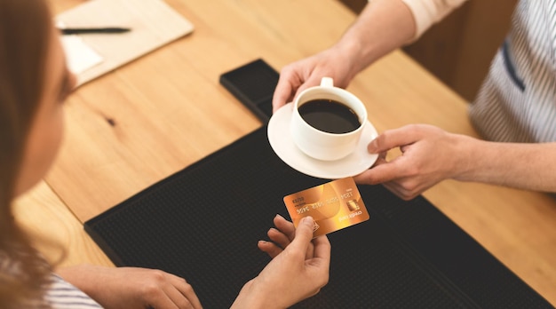 Système de paiement facile. Femme méconnaissable donnant une carte de crédit en or pour un délicieux café du matin au café, panorama