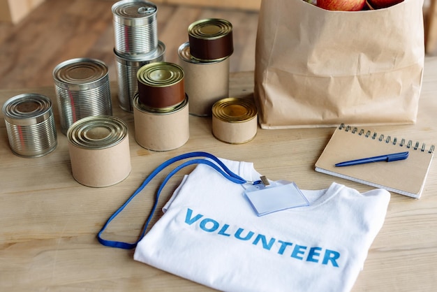 T-shirt blanc avec badge d'inscription bénévole, sac en papier et cahier sur table en bois